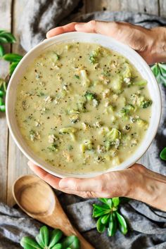 two hands holding a bowl of broccoli soup