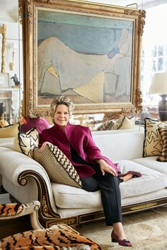 a woman sitting on top of a couch in front of a painting and leopard print pillows