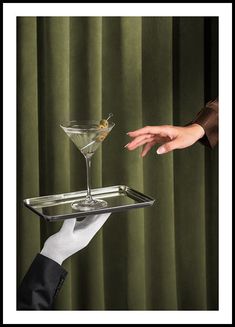 two hands reaching for a martini glass on a tray