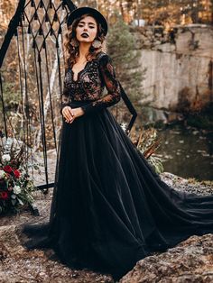 a woman in a long black dress and hat posing for the camera with her hands on her hips