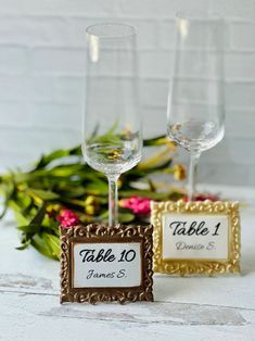 two wine glasses sitting next to each other on top of a table with flowers in the background