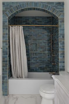 a white toilet sitting next to a bath tub in a bathroom under a blue brick wall