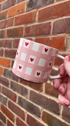 a person holding a pink and white coffee cup with hearts painted on the inside, against a brick wall