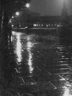 a black and white photo of a street at night with rain falling on the ground