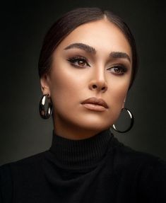 a woman wearing large hoop earrings and black turtle neck top, with her face close to the camera