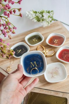 a person holding a ring in front of five different colored rings on a table with flowers