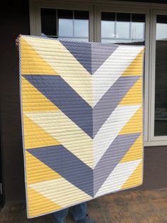 a person holding up a large quilt in front of a building with windows and doors