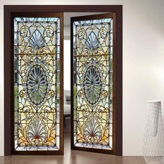 two stained glass doors in the middle of a room with a vase next to it