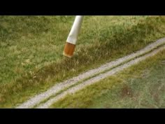 an orange and white umbrella sitting on top of a lush green grass covered field next to a dirt road