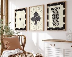 two framed art pieces hang on the wall above a wicker chair in a white room