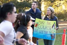 a group of people standing around each other holding a sign that says may the course be with you