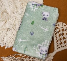 a blanket with panda bears on it next to a crochet doily and tassel