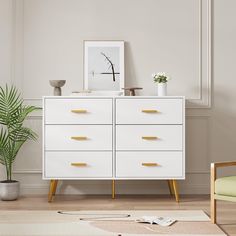 a white dresser with gold handles and drawers in a room next to a green chair