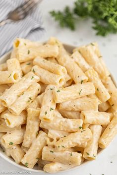 a white bowl filled with pasta and parsley on top of a marble countertop