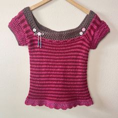 a pink and grey knitted top hanging on a hanger next to a white wall