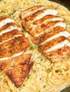 two pieces of chicken on top of pasta in a skillet