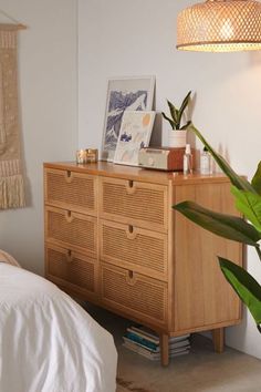 a bedroom with a bed, plant and pictures on the wall above it's dresser