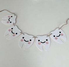 tooth shaped paper garland with pink cheeks and teeth hanging from string on white table top