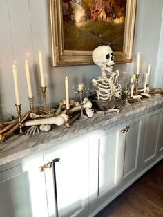 a skeleton sitting on top of a counter next to candles and other items in front of a painting