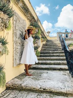 a woman in a white dress and straw hat standing on steps