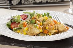 a white plate topped with chicken and vegetables next to a fork on top of a table