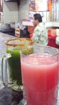 two glasses filled with liquid sitting on top of a counter next to another glass full of liquid