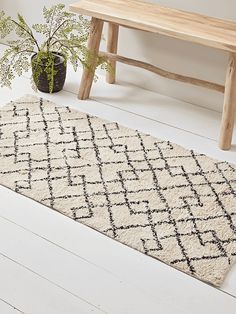 a white and black rug on the floor next to a wooden bench with a potted plant