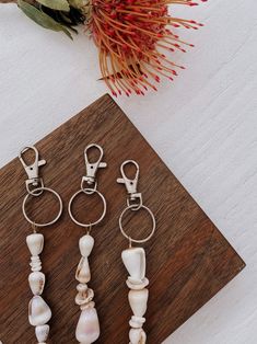 four seashell keychains sitting on top of a wooden table next to a flower