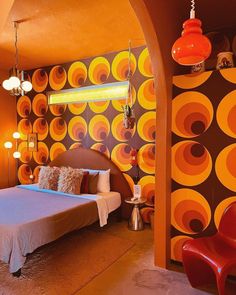 a bedroom with orange and brown circles on the wall, bed in between two red chairs