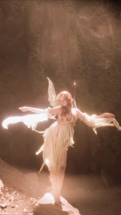 a woman dressed as a fairy standing on a rock with her arms spread out and lights in the air