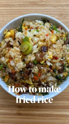 a white bowl filled with rice and vegetables on top of a wooden table next to a fork