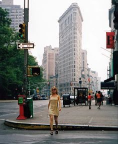 a woman walking across a street next to traffic lights and tall buildings in the background