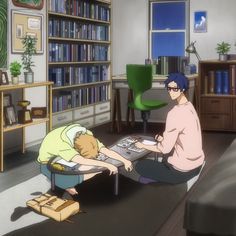 two people sitting at a table in front of a book shelf with books on it