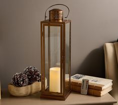 a lit candle sits on a table next to two books and a pinecone