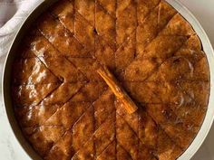 a close up of a cake in a pan on a white tablecloth with a wooden spoon