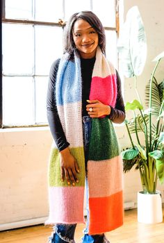 a woman standing in front of a window wearing a multicolored knitted scarf