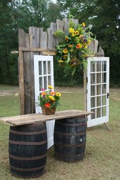 a wooden table sitting next to two barrels with flowers on them and a potted plant