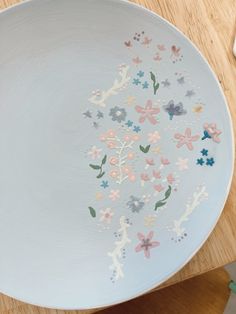 a white plate with flowers painted on it sitting on a wooden table next to a knife and fork