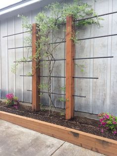 a wooden planter filled with plants next to a wall and cement slabs on the ground