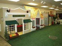 an indoor play area for children with fake houses on the floor and green roofing