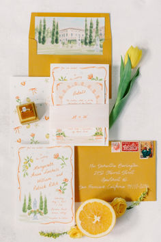 an assortment of wedding stationery items including oranges and yellow tulips are laid out on a white surface