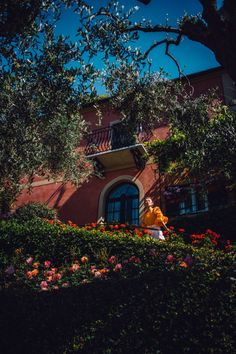 a person sitting on a bench in front of a building with trees and flowers around it