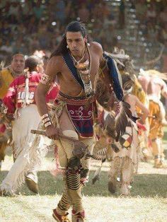 a man in native american clothing walking through the grass with other people behind him and holding onto his arm