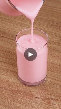 a pink liquid being poured into a glass with a video playing button on the side