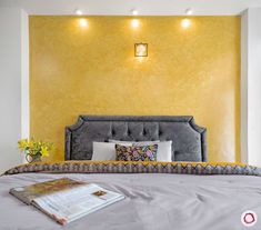 a bed with a gray headboard and pillows on top of it next to a yellow wall