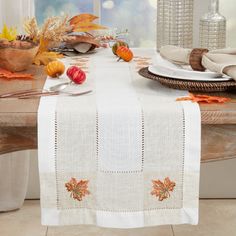 the table is set for thanksgiving dinner with white linens and autumn leaves on it