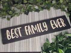 a wooden sign that says best family ever on it next to potted plants and greenery