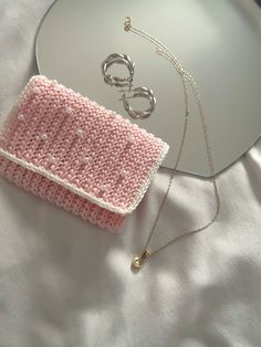 a pink knitted purse sitting on top of a white bed next to a mirror