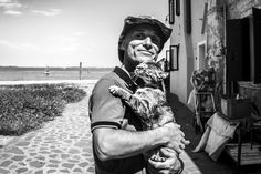 a man holding a cat in his arms while standing next to a building on the beach