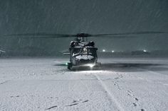 a helicopter that is sitting in the snow with it's landing gear down and lights on